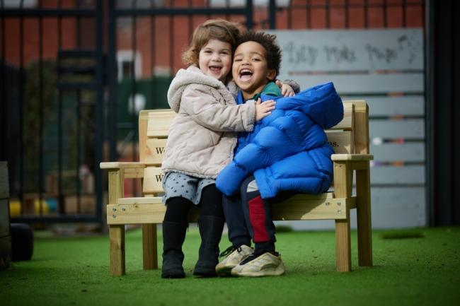 Children making friends and having fun on a buddy bench donated to Sunrise Nursery by Barratt Homes