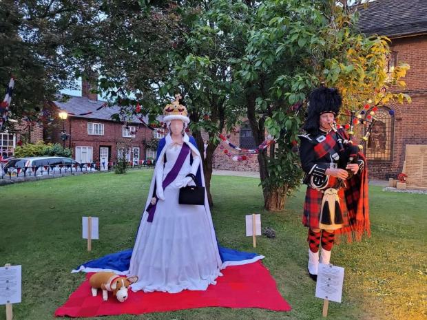 Northwich Guardian: A bugler plays beside a knitted sculpture of the Queen in the grounds of St Luke's Church in Holmes Chapel Picture: Anita Armitt